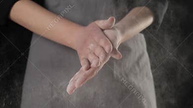Professional chef claps his hands and flour powder flies. Falling white particles on a black background. Concept of dough kneading