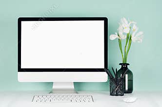 Elegant spring home workplace with blank computer screen, black stationery, keyboard, mouse, white fresh flowers in vase in green.