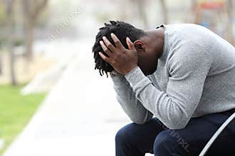 Sad depressed black man on a bench in a park