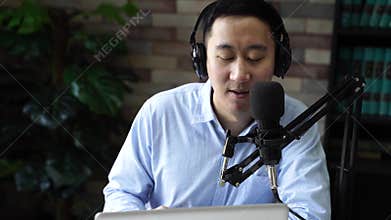 Young adult businessman podcasting and recording talk show at home studio with computer laptop on table. The desk is