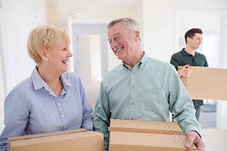 Senior Couple Downsizing In Retirement Carrying Boxes Into New Home On Moving Day With Removal Man Helping