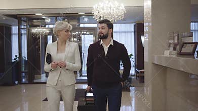 Wealthy young Caucasian couple coming to reception desk in luxurious high-class hotel. Rich clients walking in vestibule