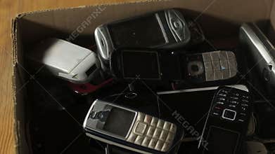 Outdated cell phones are in a big pile in a cardboard box.