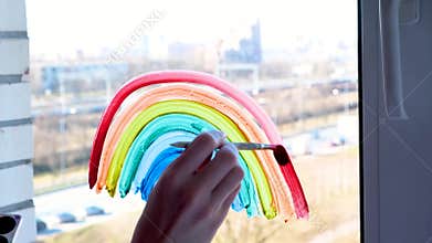 4k. Girl painting rainbow on window during Covid-19 quarantine at home. Stay at home social media campaign for