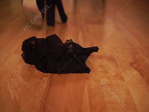 A woman in black shoes throws lace lingerie on the floor and leaves.