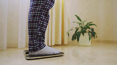 Male feet step on weighing scales. Man checking body weight in room.