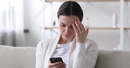 Worried young woman reading bad news in message on smartphone