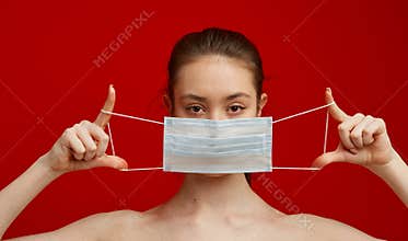 A young girl puts on a medical mask on a red background. Poster about the coronavirus COVID-19 pandemic.