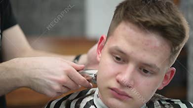 Young man's haircut in barbershop. Close-up of master clipping hair with clipper