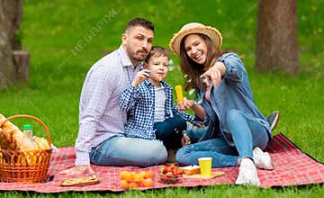 Picnic family fun. Adorable boy with his mom and dad blowing soap bubbles in coutryside on summer day
