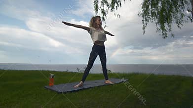 Young fit woman practice yoga on coast near the lake or sea. Woman doing Five Pointed Star pose