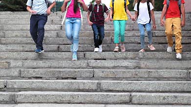 Happy schoolchildren run down stone stairs on sunny day