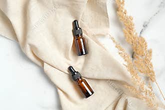 Amber glass essential oil brown bottles with beige fabric and dry flowers on marble background. Flat lay, top view. Natural