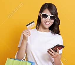 Happy young woman in summer dress and using mobile phone shopping online with credit card