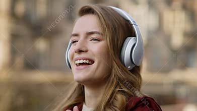 Happy woman listening music headphones outdoors. Smiling girl dancing on street.