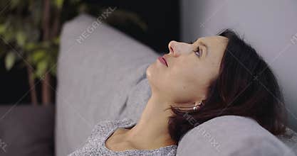 Tired woman taking break on sofa between domestic chores