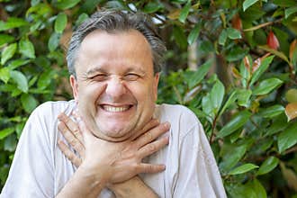 A white man makes a funny face while clutching his neck with his hands as if he wanted to choke