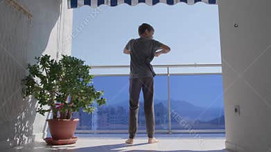 Kid doing sport exercises, crouching on the balcony. Sport, healhty lifestyle, active leisure at home