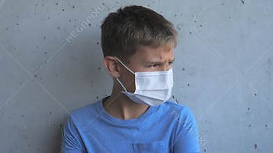 Boy with medical protective mask looking at camera and turns his head to the side. Kid standing near grunge gray wall