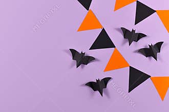 Halloween background with garlands and paper bats in traditional colors orange and black on violet background