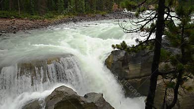 Mountain river rushing over rocks as rapids and small waterfall.