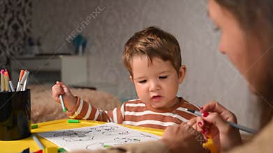 Child paints coloring book with mother. Fun educational games