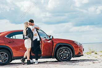 Woman and handsome man kissing and hugging near car