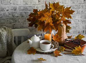Bouquet of maple leaves, pumpkin, hot tea, lighted candle on the kitchen table.Warm cozy autumn interior