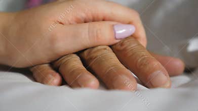 Granddaughter takes and gently touches wrinkled arm of sick mature grandma lying in bed hospital. Girl comforts hand of