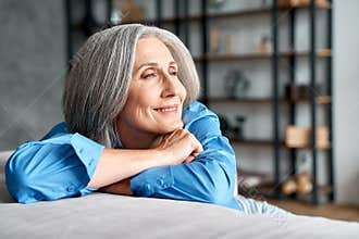 Happy relaxed mature old woman resting dreaming sitting on couch at home.
