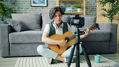 Slow motion of teenage blogger talking for camera holding guitar at home