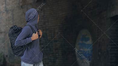 Thoughtful black teen in hoodie with backpack walking dangerous city suburb