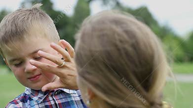 Woman puts protective cream on the boy's face, the boy does not like it, he turns away