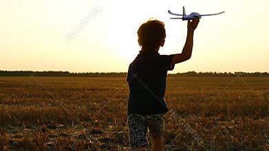 The boy runs through the wheat field after the harvest. The child holds a toy plane in his hand and imagines flying