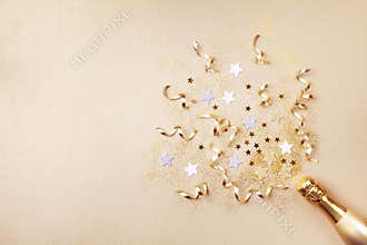 Champagne bottle with confetti stars, glitter and party streamers on golden background. Christmas, birthday or wedding. Flat lay