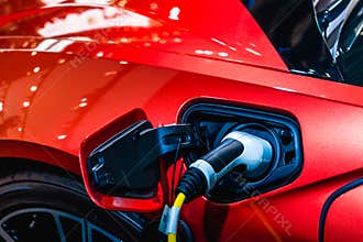 Red EV Car at charging station with the power cable supply plugged in. Power supply connect to electric vehicle for charging the