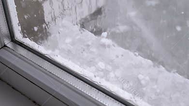 Hail outside the window. Pieces of hail fall on the windowsill behind a plastic window
