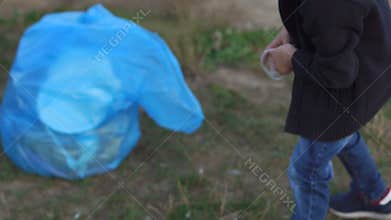 A little boy collects garbage on the beach by the river or lake in the park.