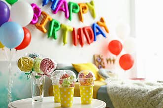 Table with treats and phrase HAPPY BIRTHDAY made of colorful balloon letters in modern bedroom
