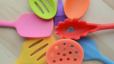 Rotation of bright multi colored kitchen utensils on wooden background