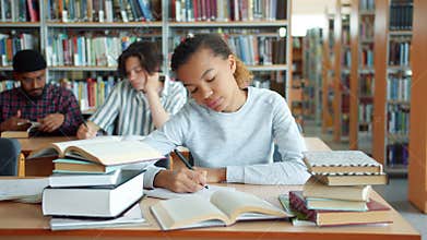 Tired African American girl studying in college library writing reading books