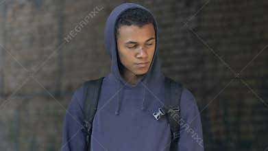 Sad african american hooded teen with face scar and backpack walking ruins alone