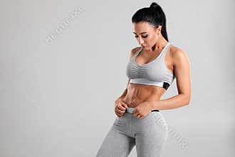 Fitness woman showing abs and flat belly,  on gray background. Beautiful athletic girl, shaped abdominal