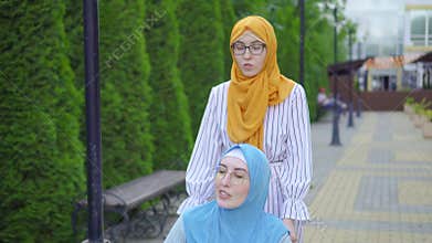 Young muslim disabled in a traditional scarf in a wheelchair communicates with a muslim friend on the street close up