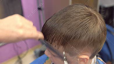 Hairdresser cuts bangs with scissors on boy`s head. Stylist`s hands close-up, top view.
