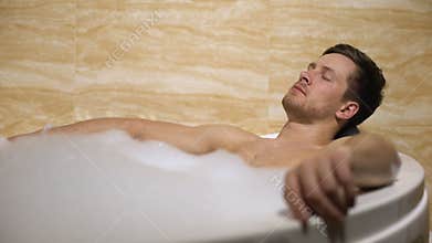 Handsome man enjoying aroma and hot water, taking bath with foam, leisure