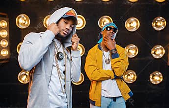 Two black rappers in caps on stage with spotlights