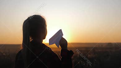 Happy little girl playing with a paper airplane outdoors during sunset. Concept big child dream.