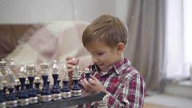 Close-up of cute Caucasian boy sitting in front of chess board and smiling. Clever child enjoying his hobby indoors
