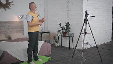 Influencers blogger, aged man shows an exercise for joints on phone camera recording sport vlog for social networks and